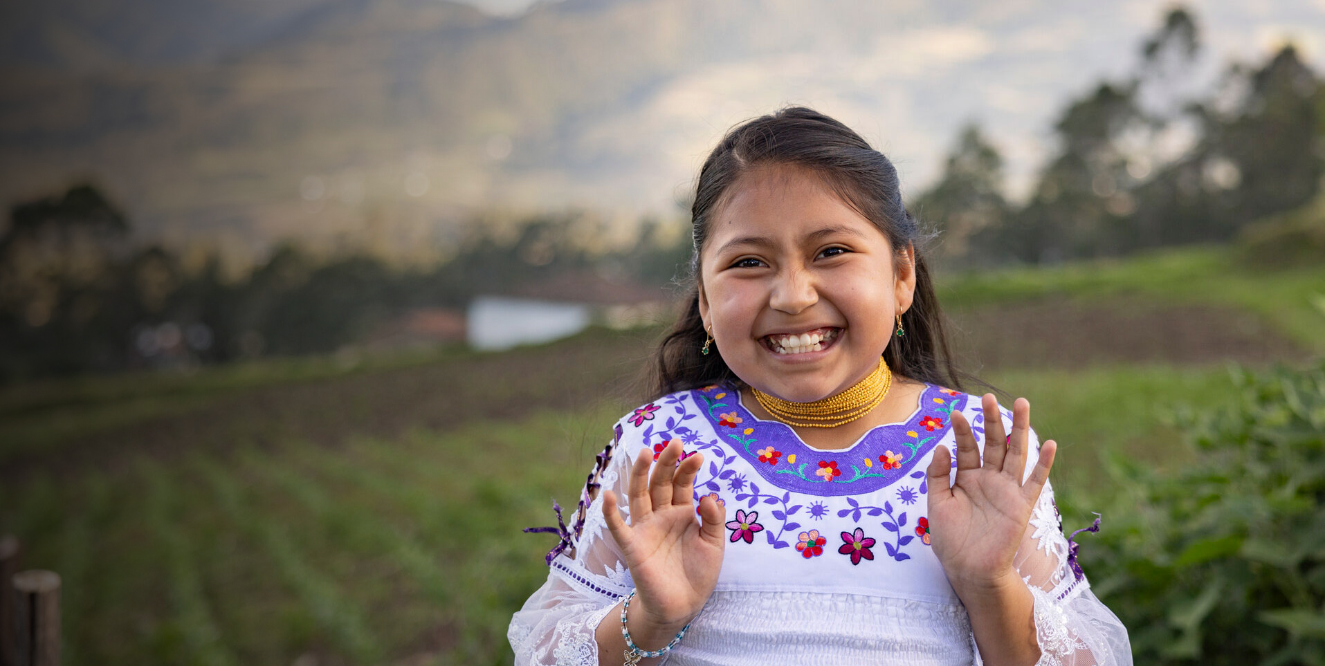 ChildFund Village - Girl Smiling, purple dress, scenic mountain background