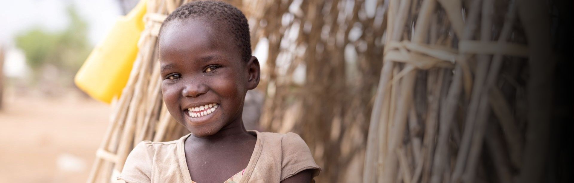 A young girl smiles in front of her house.