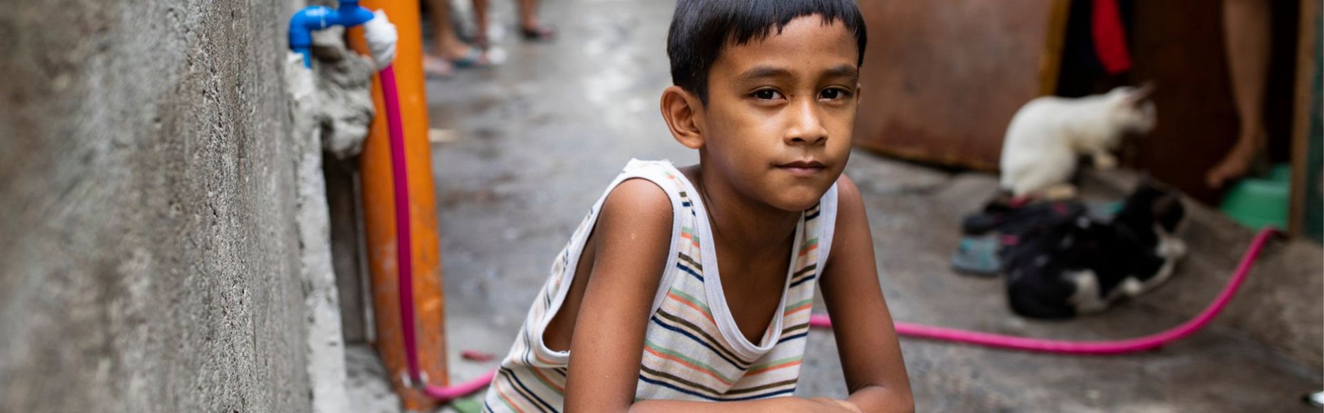 A boy in the Philippines crouches in a deserted alleyway, looking thoughtfully at the camera.