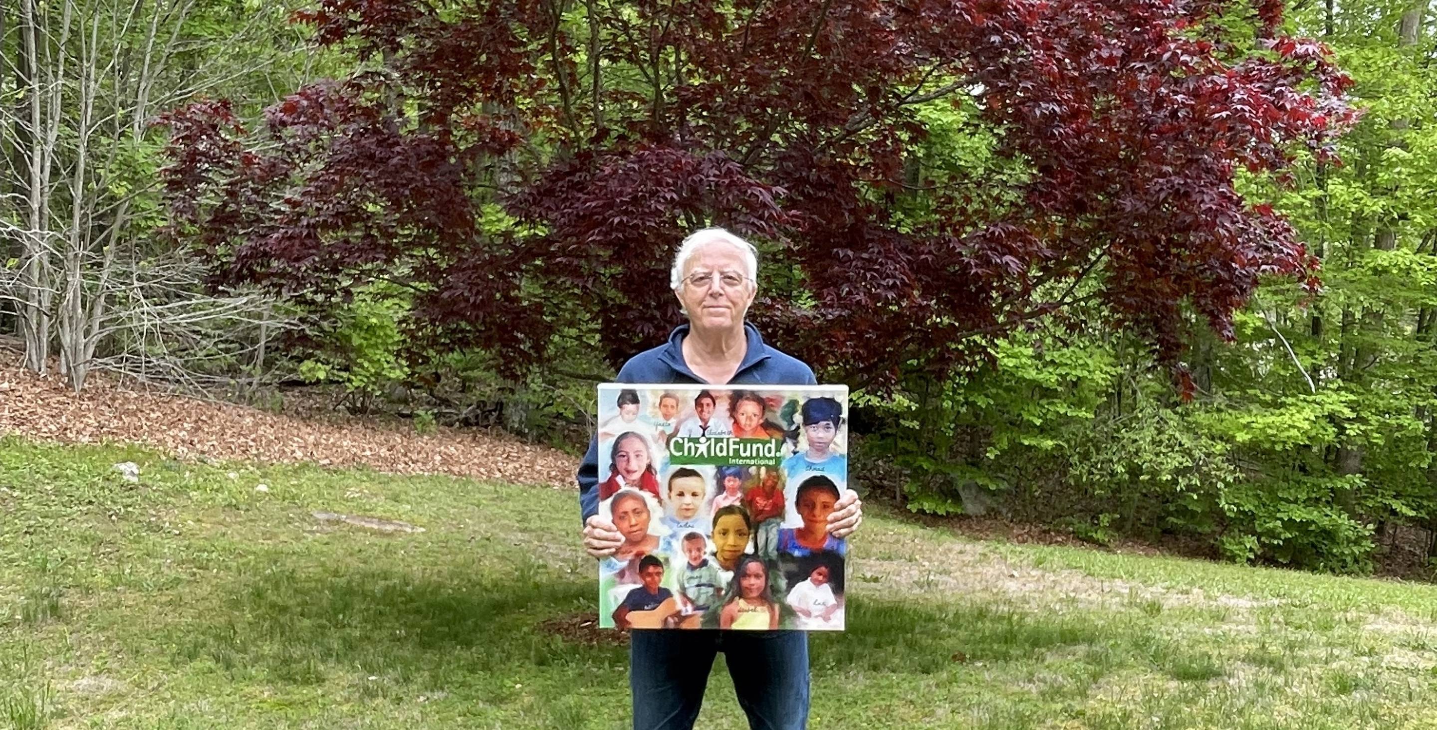 A man stands in a field holding a large sign that says 