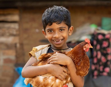 Smiling boy holds a chicken his family received though ChildFund