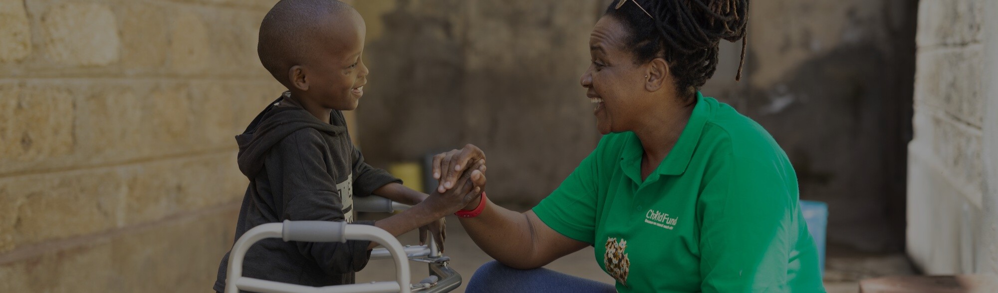 Hero image of childfund staff interacting with a child with a walker.