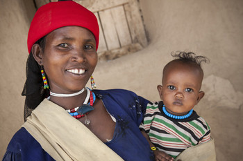 A mother, smiling, holds her child in Ethiopia. 