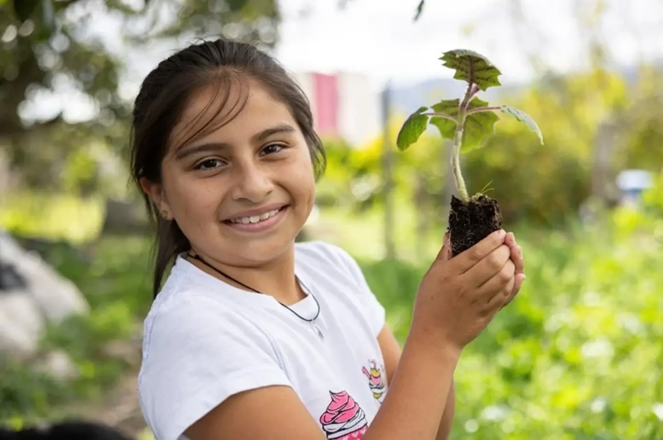 A girl smiles while holding a small plant.