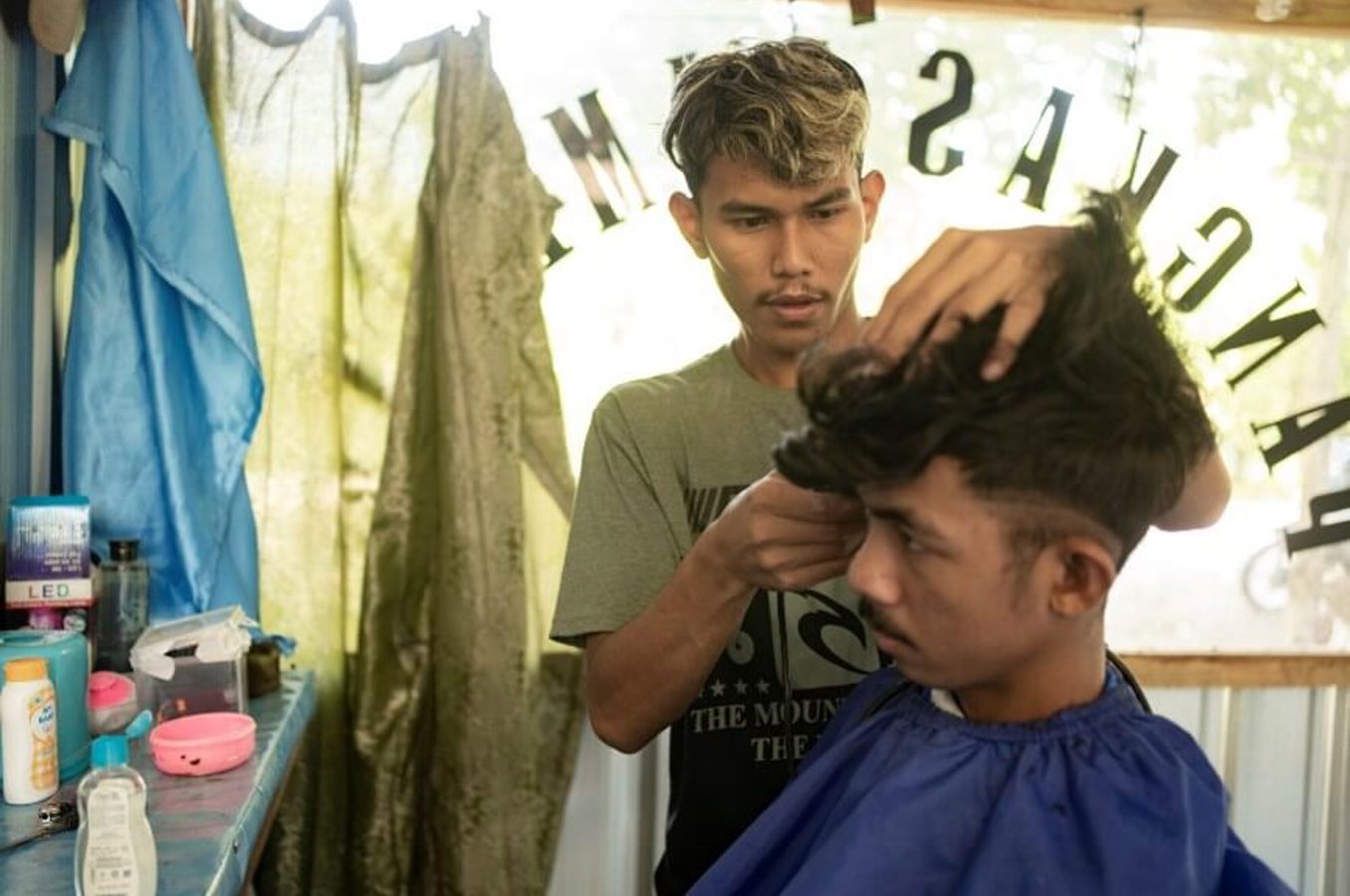 Young man cuts a clients hair in shop
