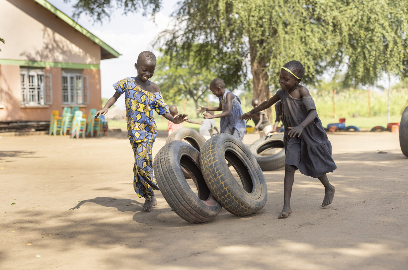 Two girls in Uganda chase a tire around a playground.