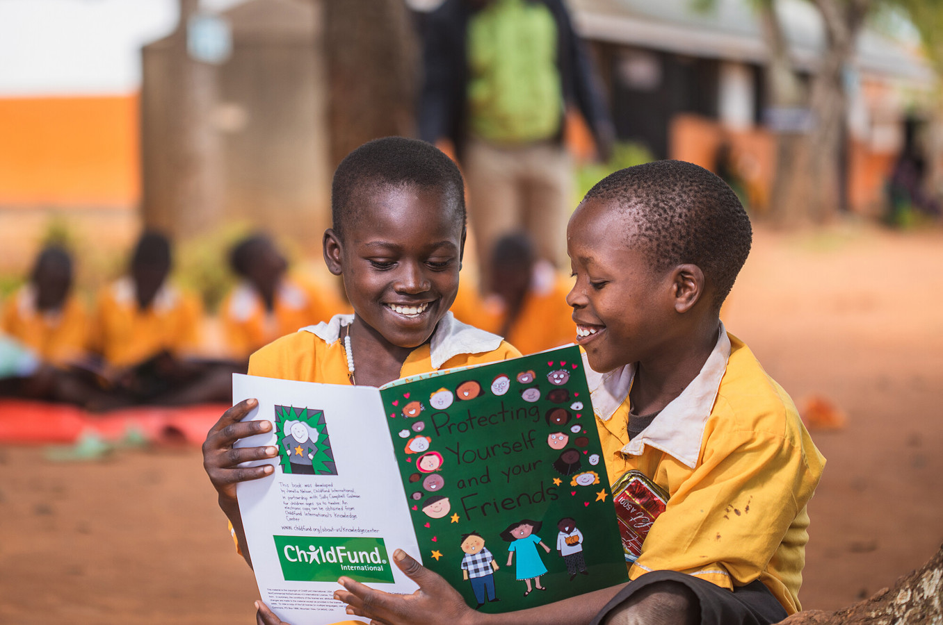 Two little boys in Uganda smile as they read a book entitled 