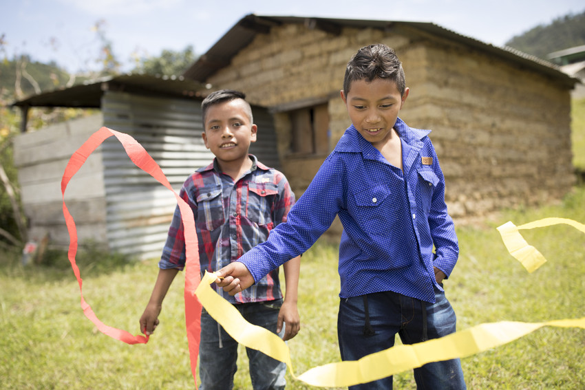 Two boys standing outside in Guatemala playing, waving red and yellow streamers in the air.