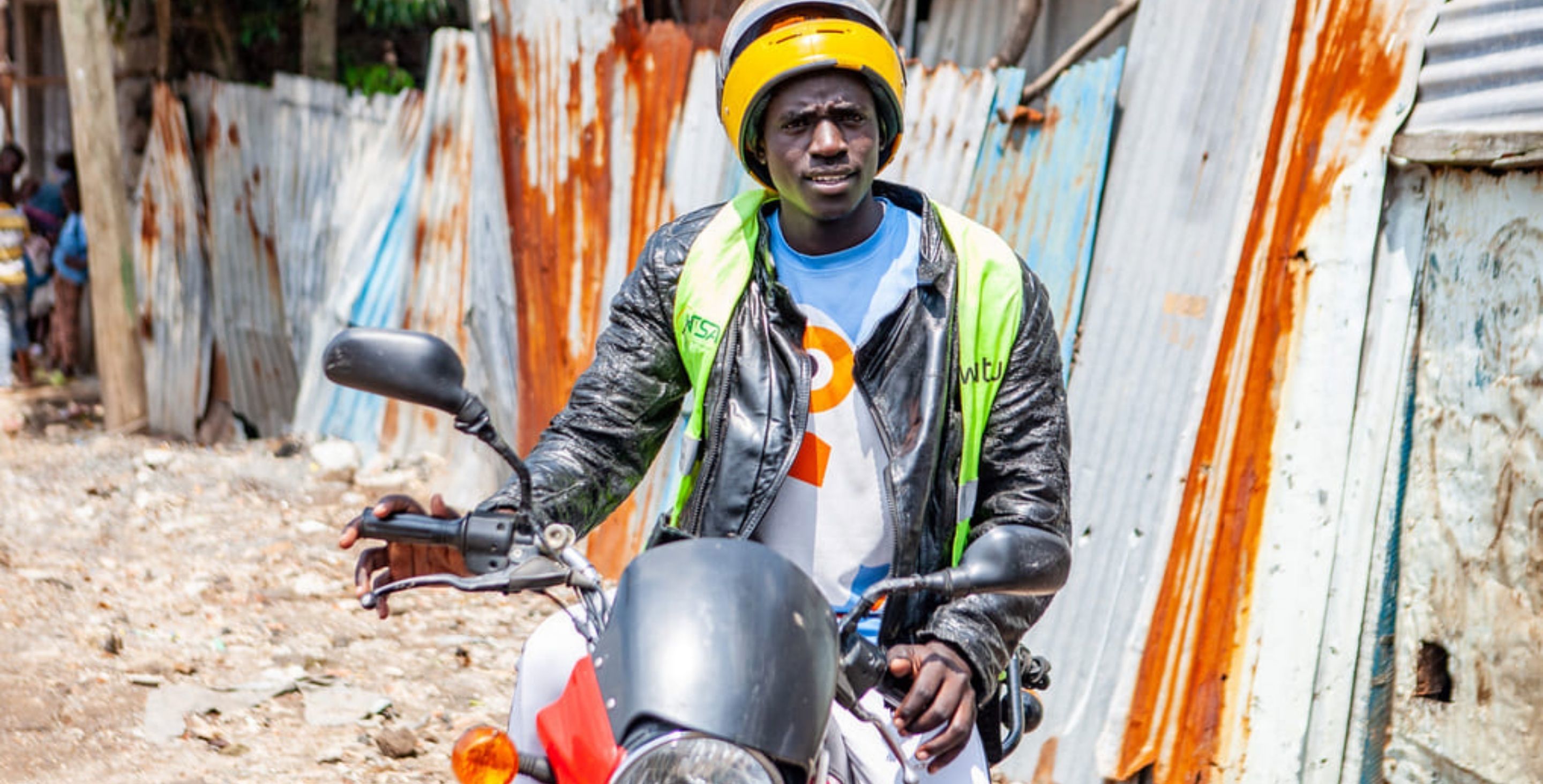 A man in Kenya sits on a boda boda in a crowded city, wearing a ChildFund vest.