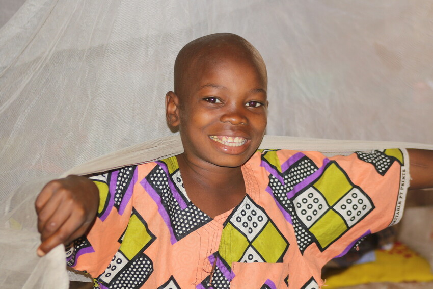A child in The Gambia smiles in front of a mosquito net.