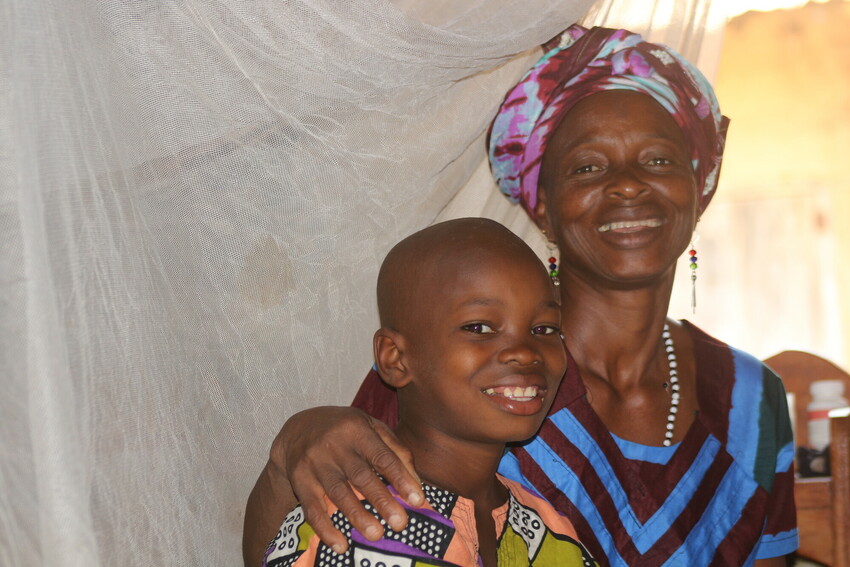 A child in The Gambia smiles next to his mother.