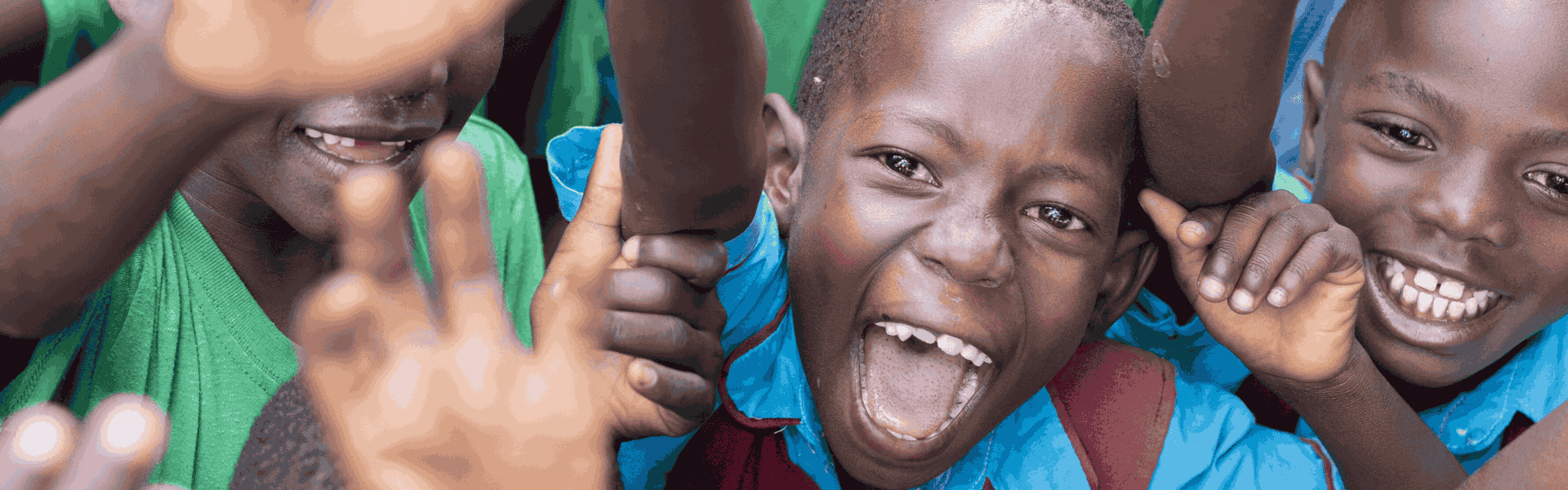 A group of children in Uganda wearing school uniforms cheer while laughing at the camera.