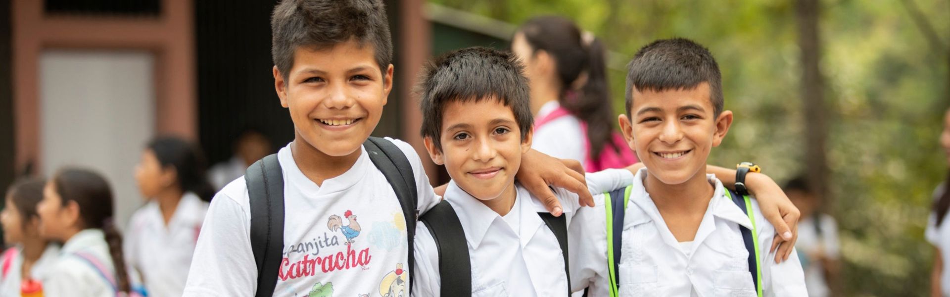 Three boys wearing school uniforms and backpacks pause for a photo.