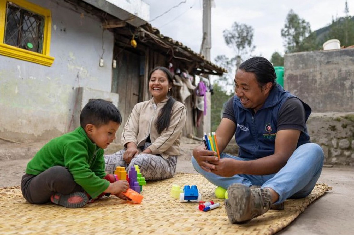 Smiling ECD student and ChildFund staff member play with blocks outside 