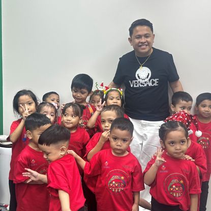 A man in the Philippines stands in a room with a group of small children, smiling.