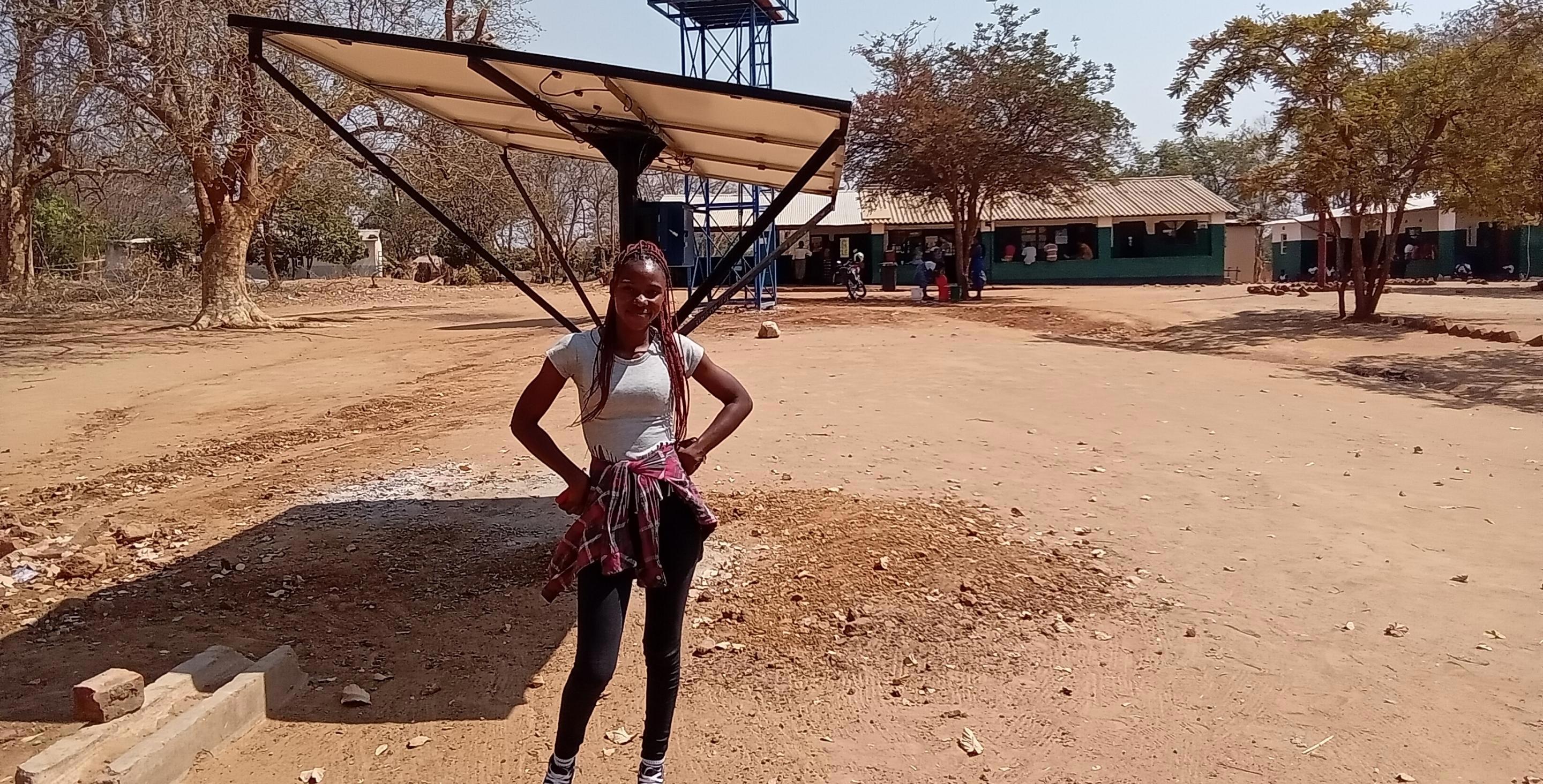A young woman in Zambia stands in front of a water tower in her community.