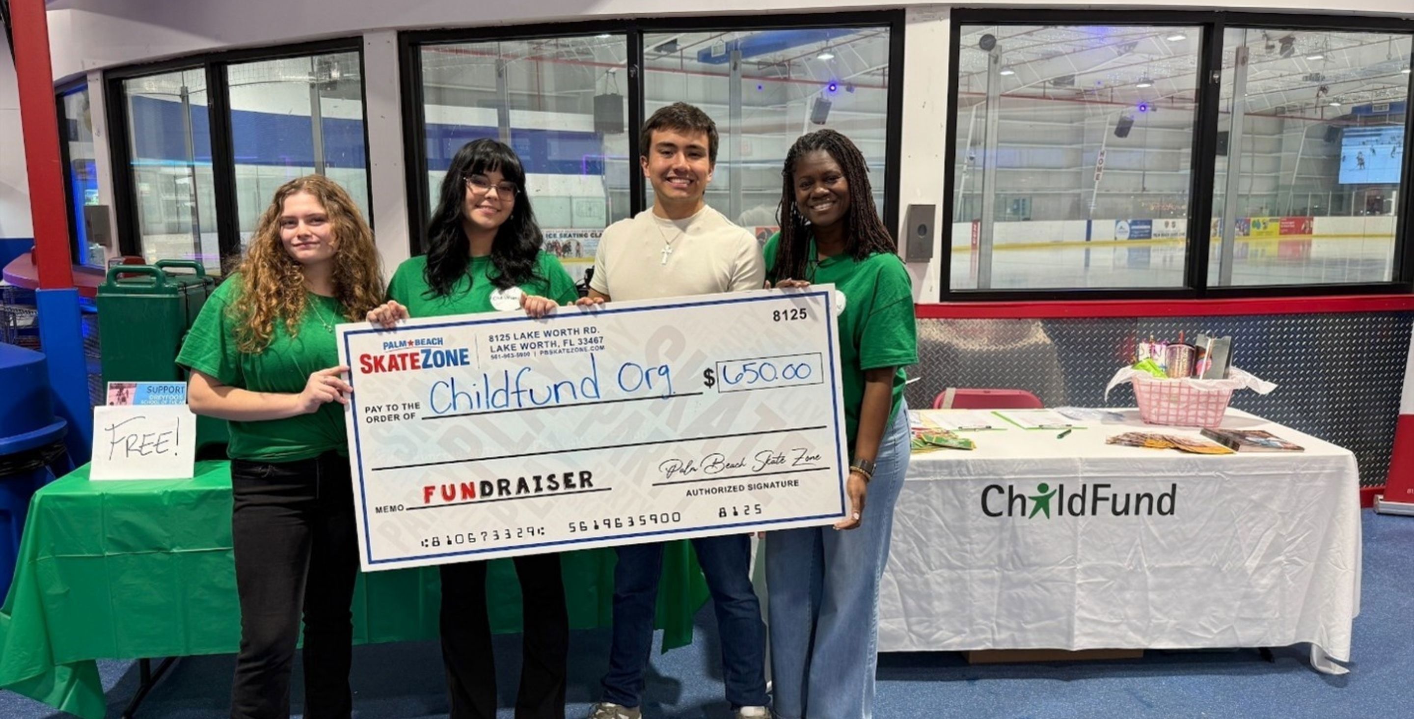 A group of high school students stand in front of an ice skating rink holding a large check made out to ChildFund for $600.