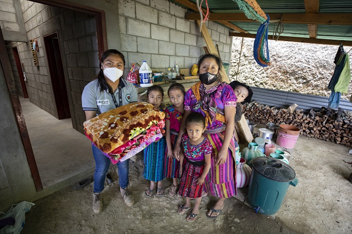 Family stands together as they receive blankets from a woman wearing a ChildFund shirt.