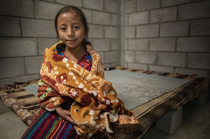 Girl smiles slightly at camera while wrapped in a blanket.