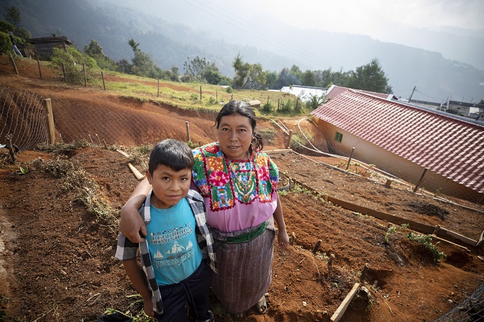A mother and son stand in a terraced garden in Guatemala, smiling slightly at the camera.