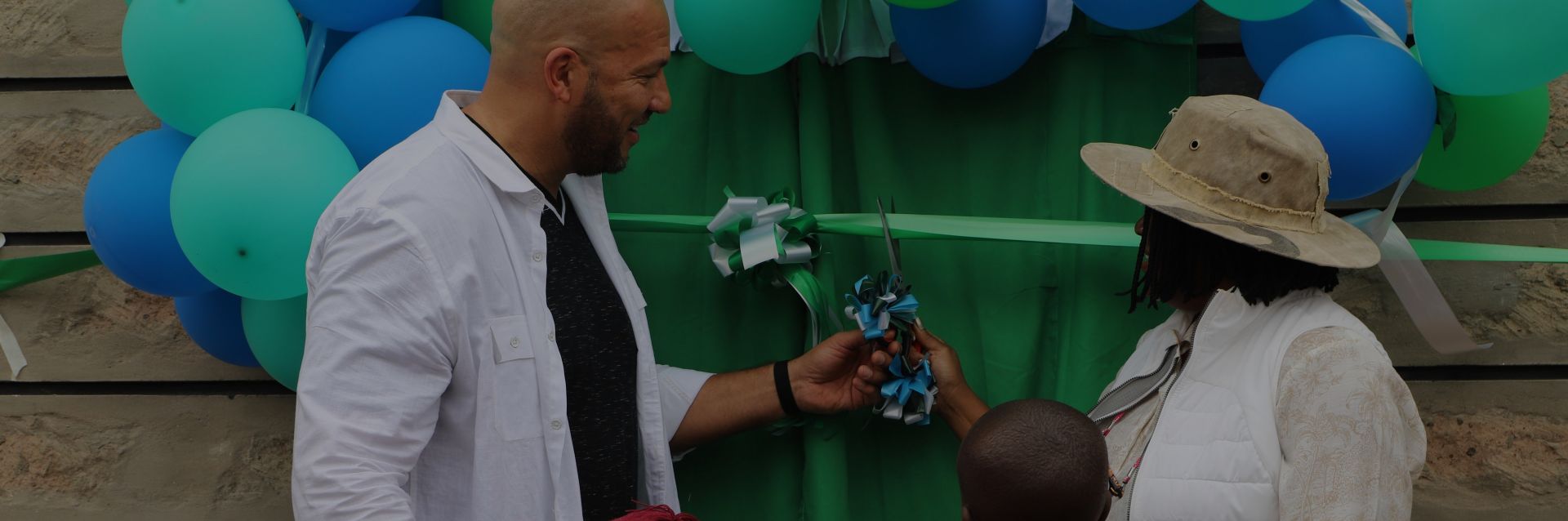 A man and a woman cutting a ribbon at a community center opening ceremony, with two children watching.