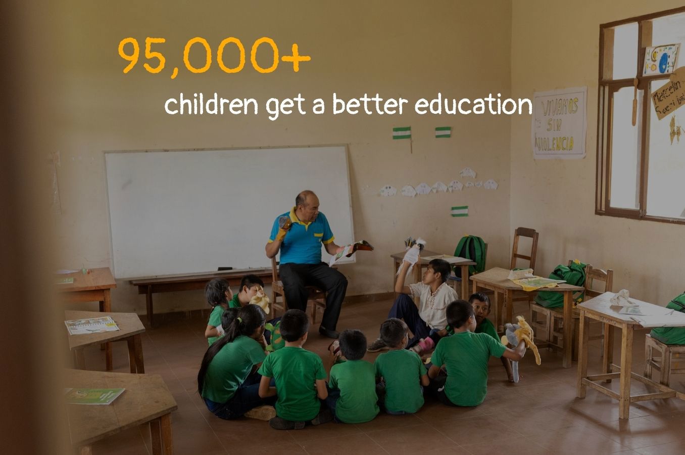 A photo of children sitting on the floor of a classroom. Text on the photo reads 