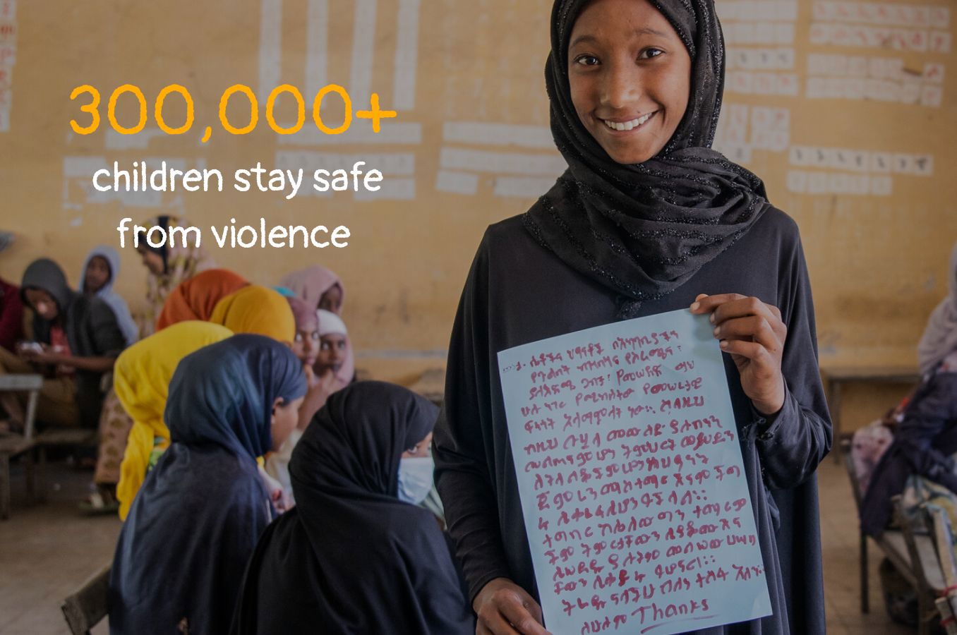 Photo of a girl standing in a classroom, smiling. Text on photo reads 