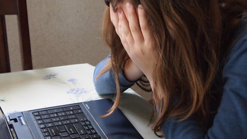 A girl sits at a table, holding her face in her hands.