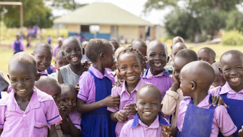 Children in Uganda wearing purple uniforms gather outside together for a photo, smiling