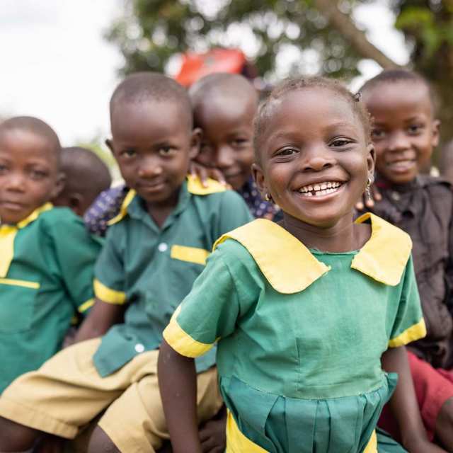 Smiling preschool-age girl in Uganda, with several classmates behind her, all in uniform