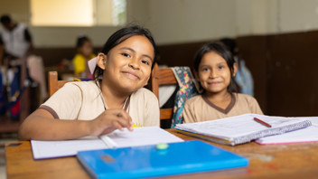 Two girls in Bolivia sit at a desk, studying and smiling slightly at the camera