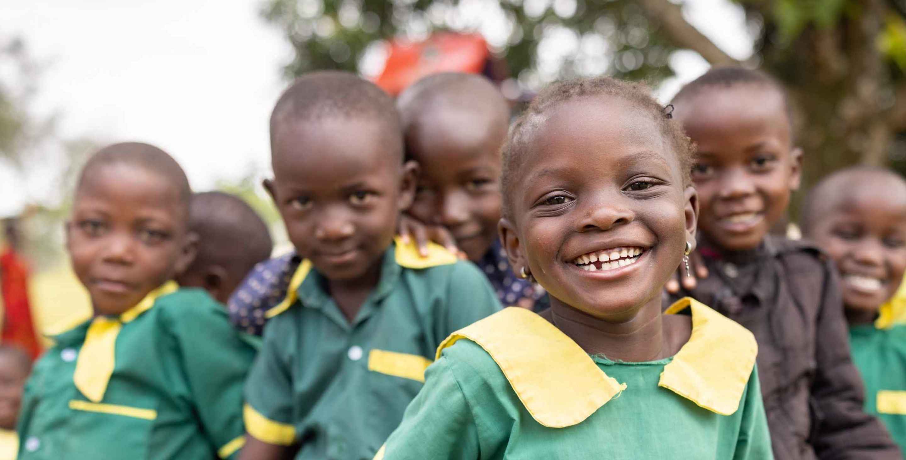 Smiling little girl in school uniform, a bunch of her classmates in the background