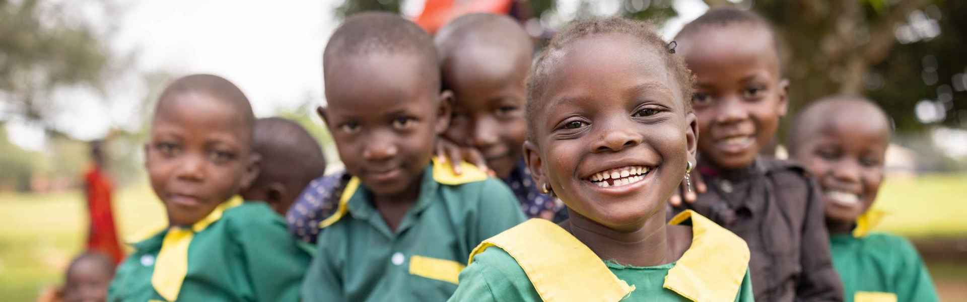 Smiling little girl in school uniform, a bunch of her classmates in the background