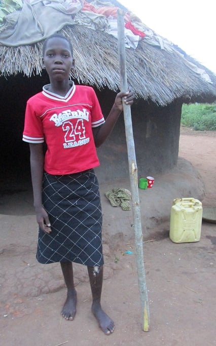 Teenage girl red shirt standing outside in Uganda leg injury walking stick. 