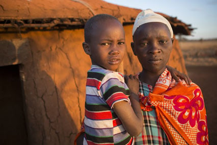 A mother holding her daughter outside mud house in Kenya.