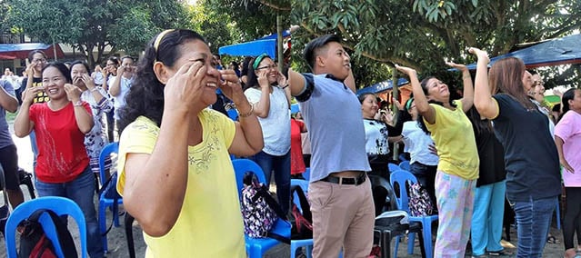 A group of men and women laugh while doing stretches together outdoors in the Philippines.