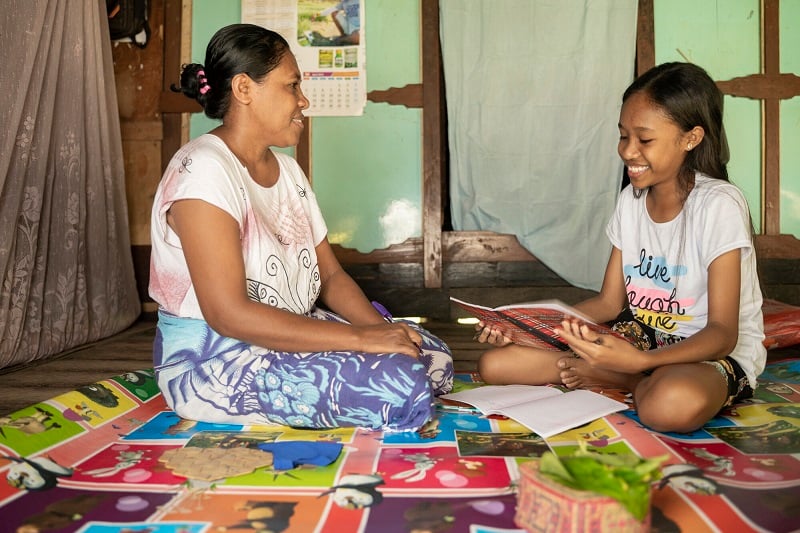 An Indonesian mother and daughter sit on the floor indoors.