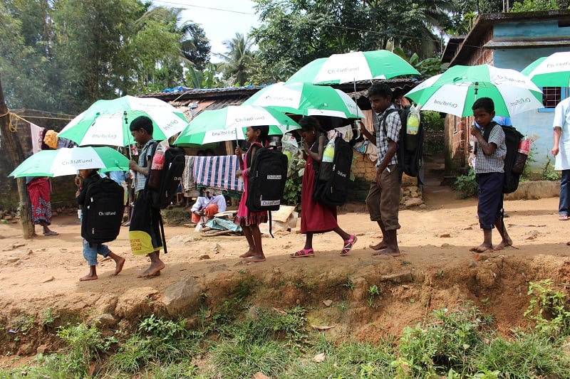 Indian schoolchildren walk with green and white umbrellas.