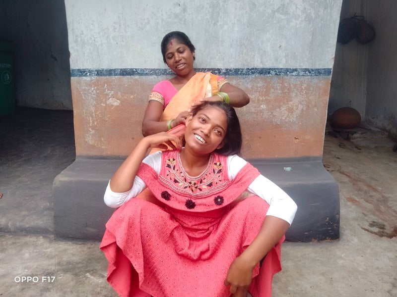 An Indian schoolgirl smiles as her mother styles her hair.