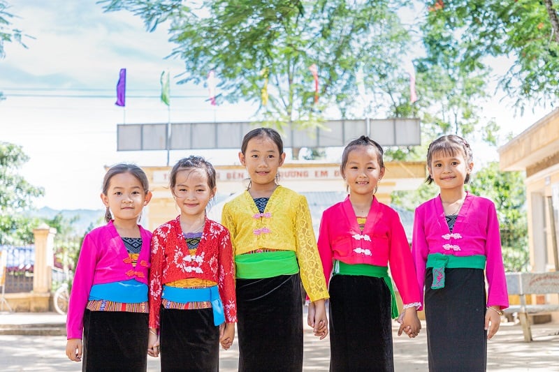 Girls in Vietnam dressed in bright colors hold hands and smile.