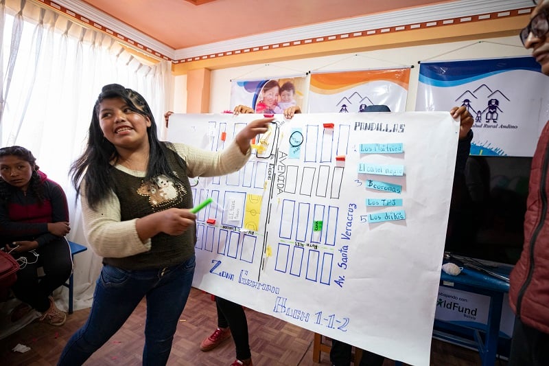 A young woman in Bolivia gestures to a map of her community, smiling.
