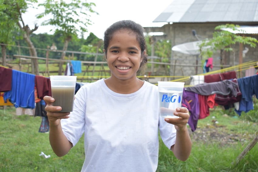 Young girl in Indonesia holds one cup of dirty water and one cup of clean water.