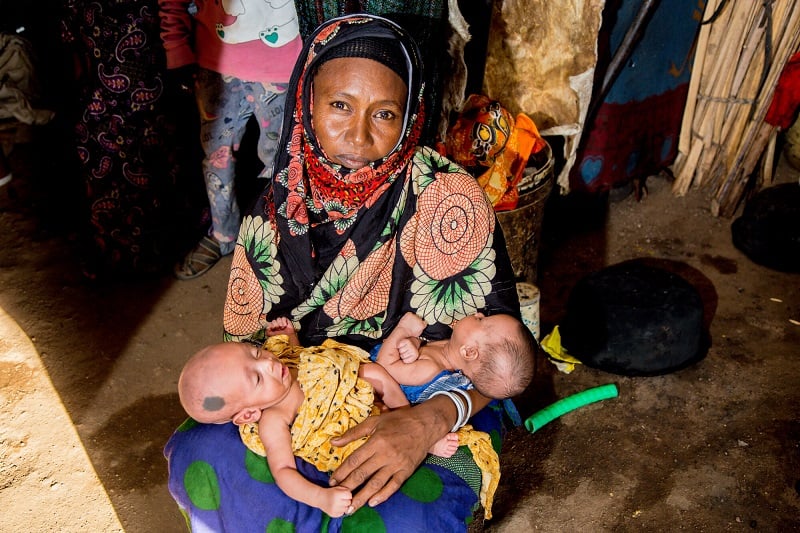 Mother in Kenya holds twin babies, looking up at camera.