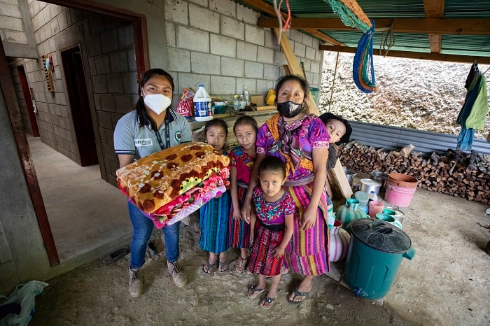 Family stands together as they receive blankets from a woman wearing a ChildFund shirt.