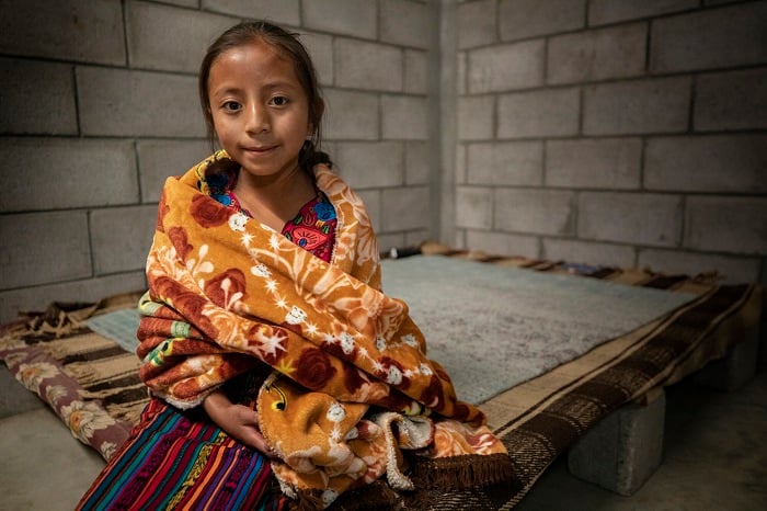 Girl smiles slightly at camera while wrapped in a blanket.