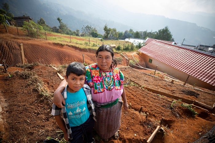 A mother and son stand in a terraced garden in Guatemala, smiling slightly at the camera.