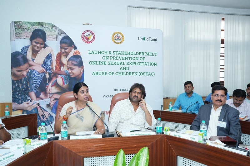 Adults sit in a meeting room in India with a sign about the ChildFund online safety campaign behind them.
