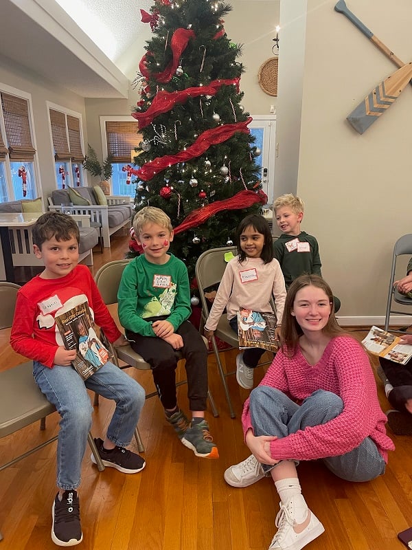 A group of students sit in front of a Christmas tree with ChildFund's Real Gifts Catalog, smiling at the camera.