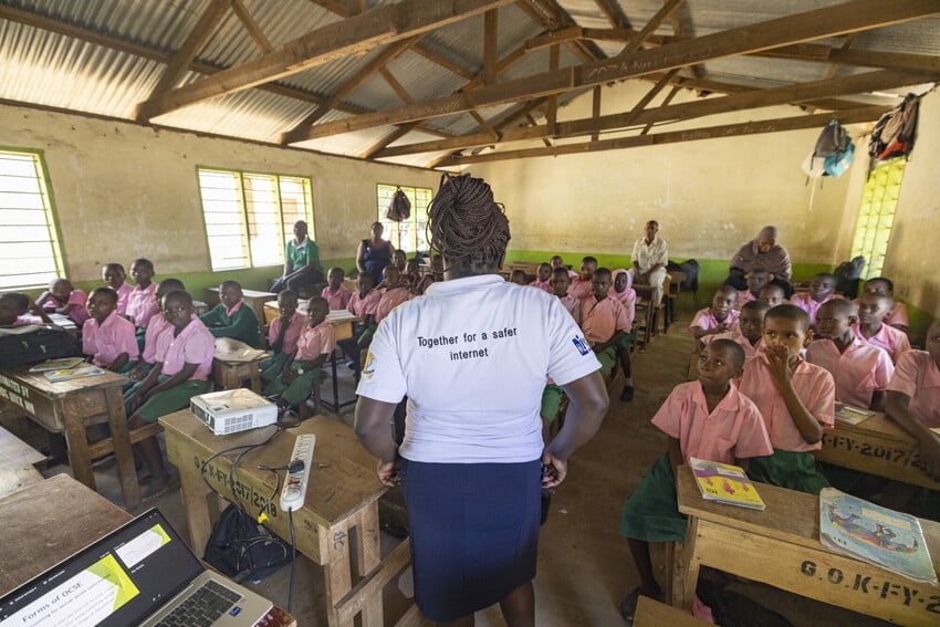 Woman stands up in a classroom in Kenya wearing a shirt that reads, "Together for a safer internet."