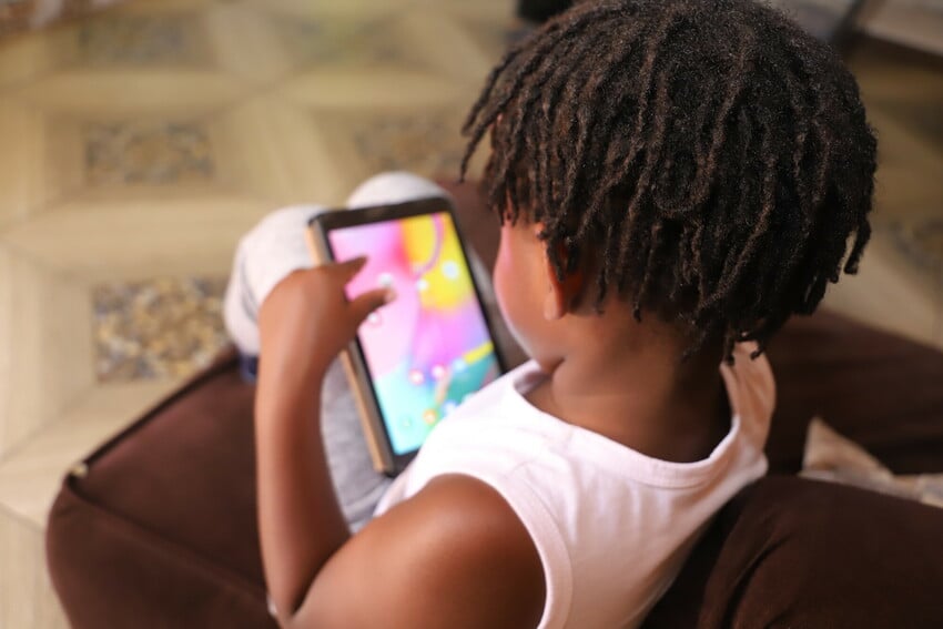A child scrolls on a tablet, only the back of their head showing.
